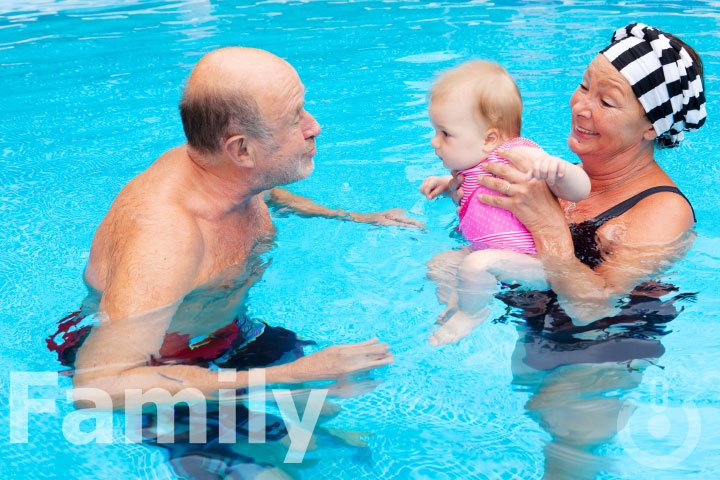 Older man and woman in a pool with an infant girl